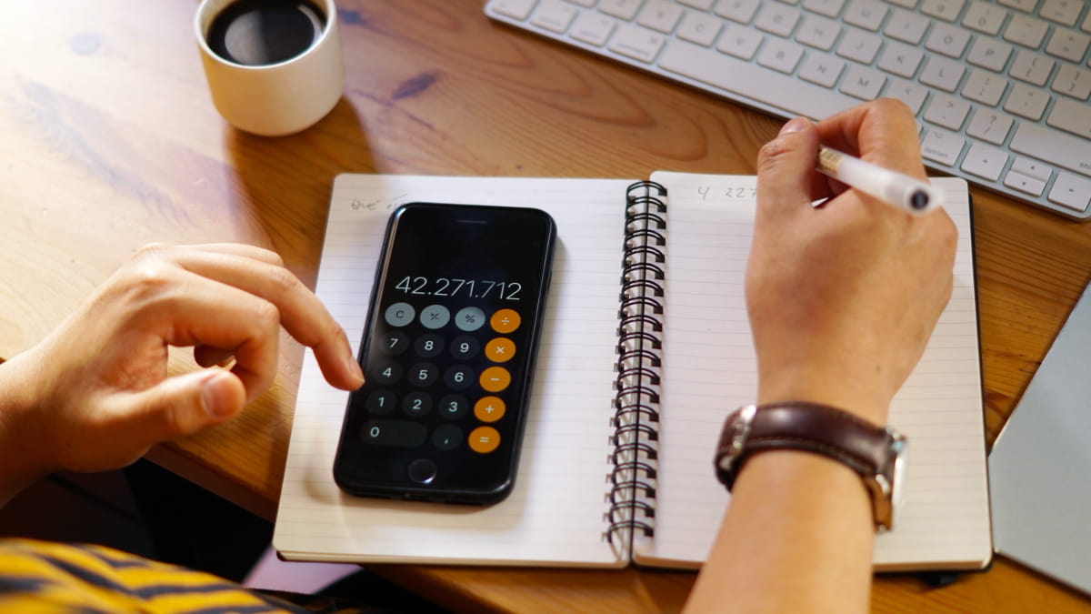 personne calculant sur son smartphone en prenant des notes