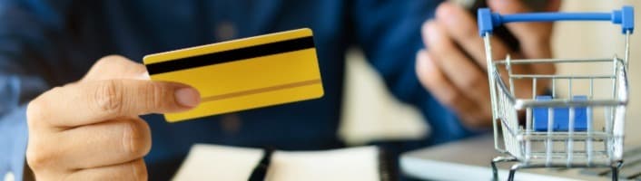 main tenant une carte bancaire jaune et à côté un caddie miniature