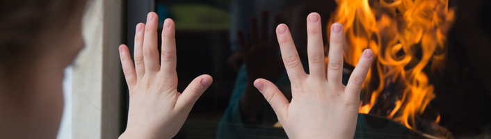 mains d'un enfant posées sur la vitre d'un poêle